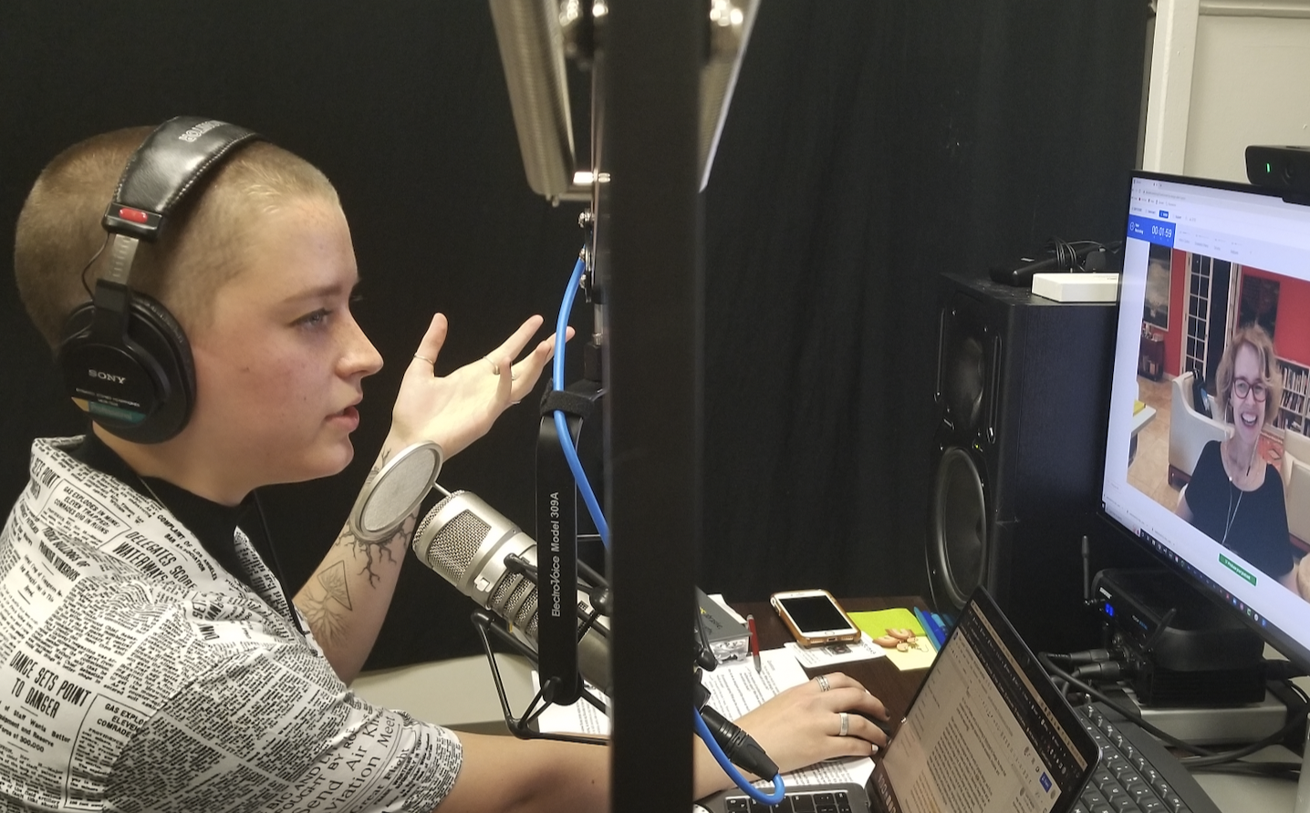 Lynn is to the left in front of a dynamic studio mic, looking at the computer screen as they talk and motion with one hand. Ellen Lupton, the guest on screen, has her head slightly tilted as she listens with a grin.