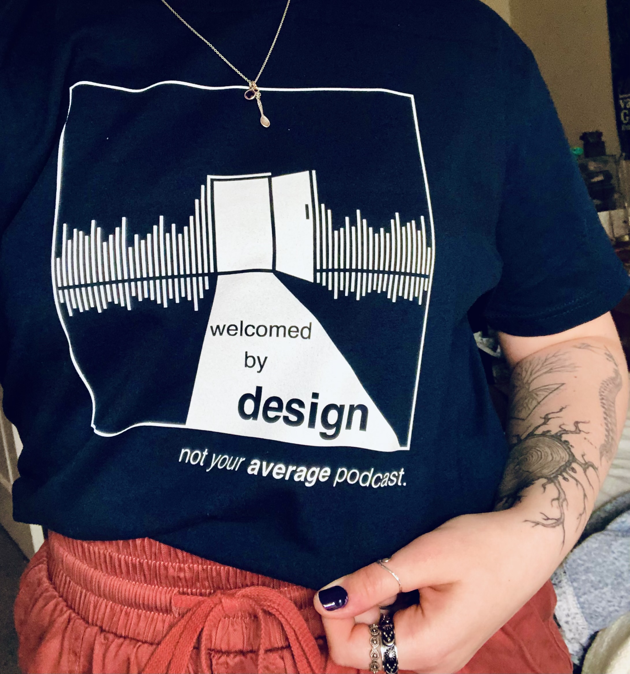 Welcomed by Design cover art on a shirt, with the tagline 'not your average podcast' below it